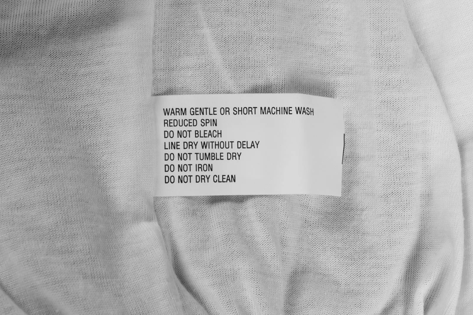 A printed care label sewn into white knit fabric, listing washing, drying and ironing instructions