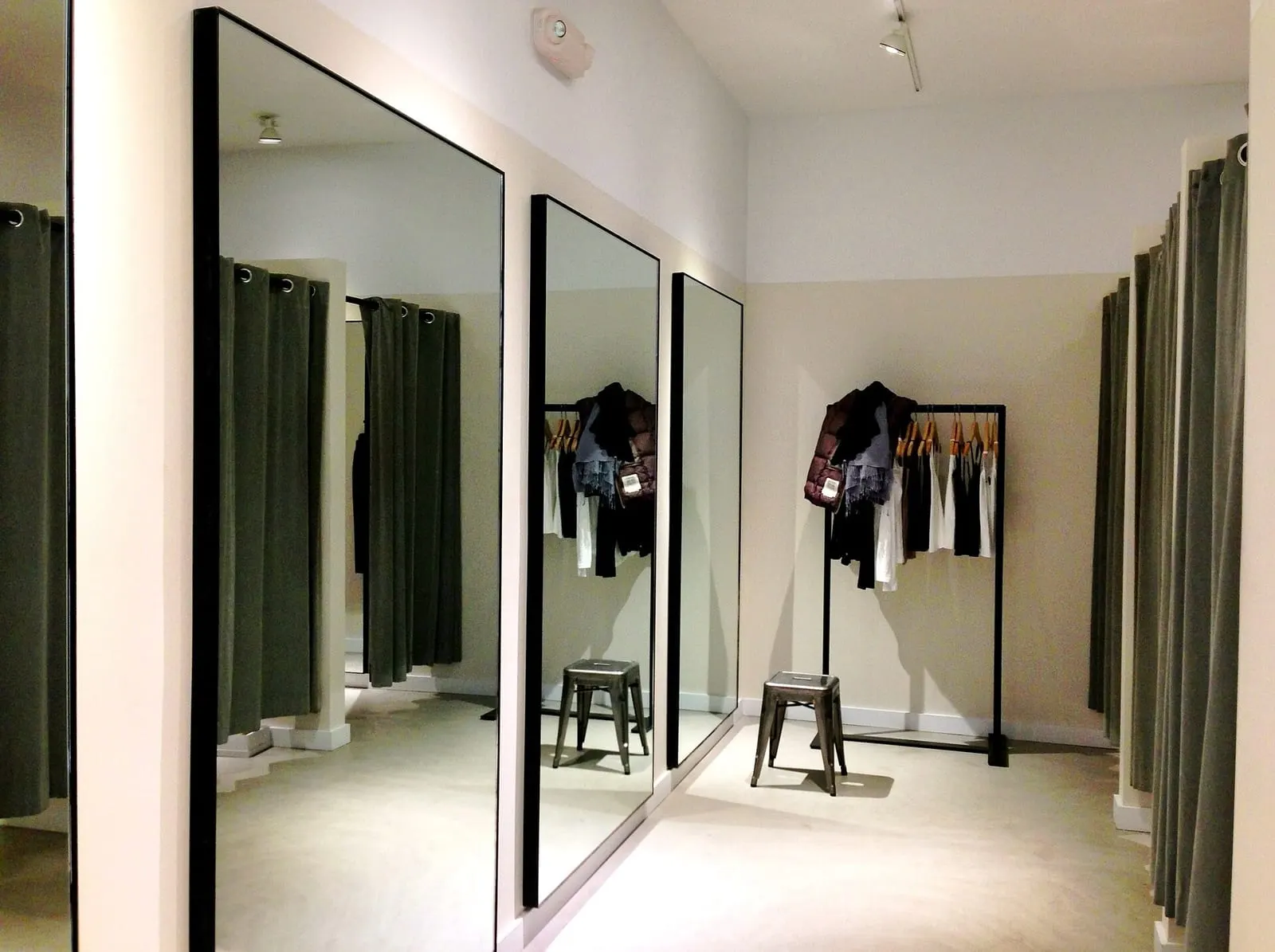 A bright fitting room with full-length mirrors, curtained cubicles and a rail of garments on hangers