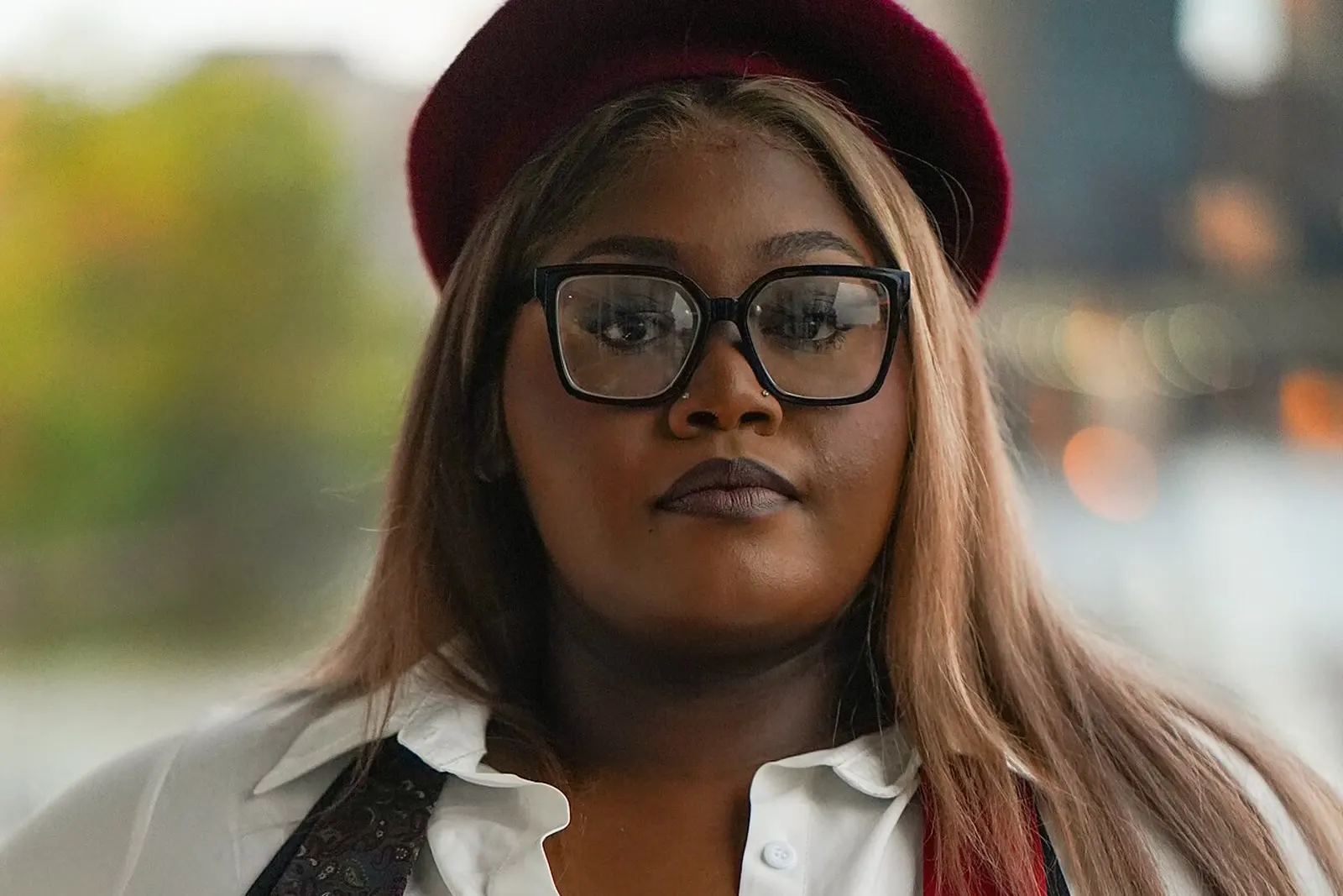 A plus-size model in a white shirt, black waistcoat and deep red hat