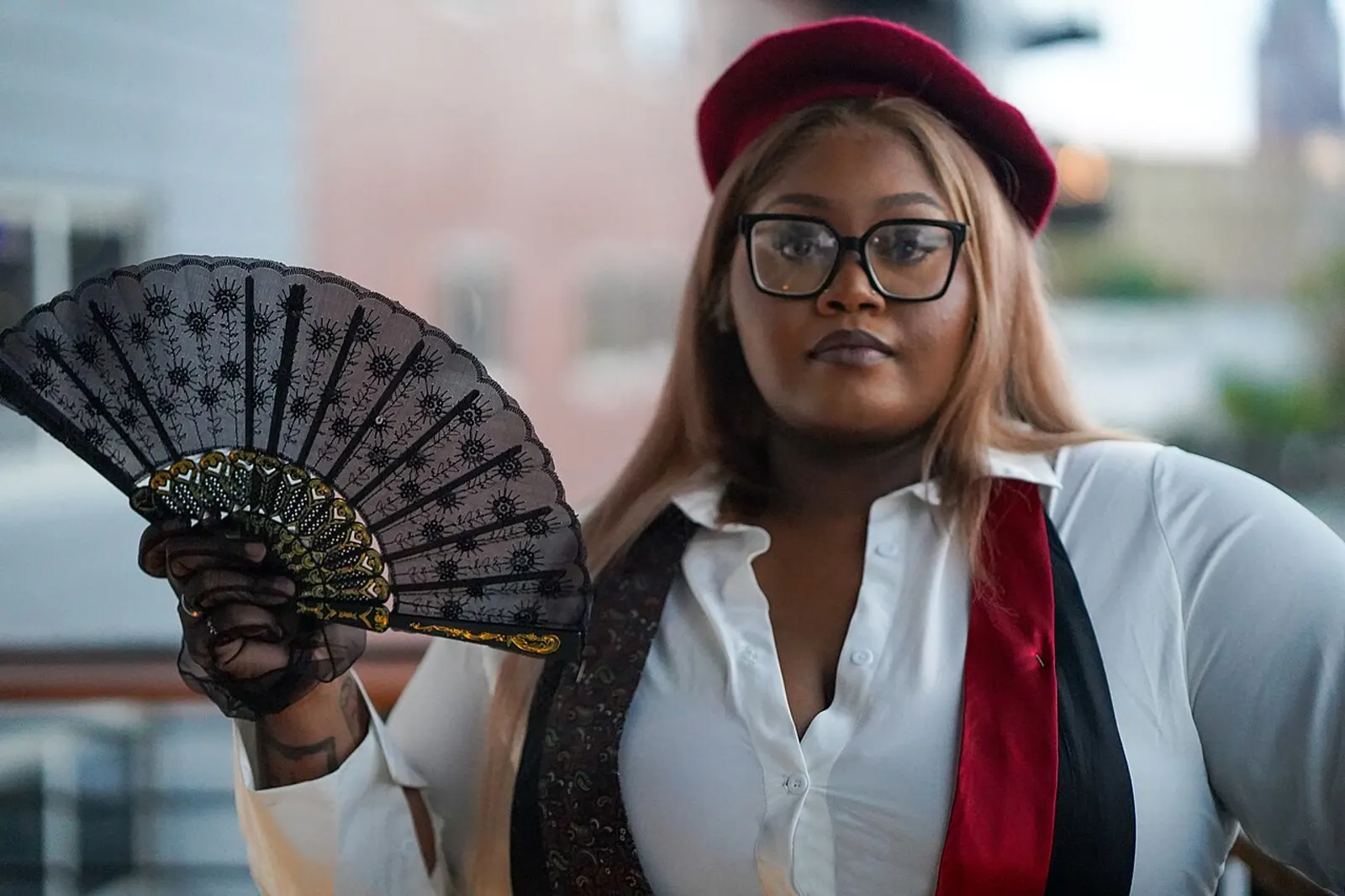 A plus-size model holding a lace fan, wearing a white shirt and deep red hat