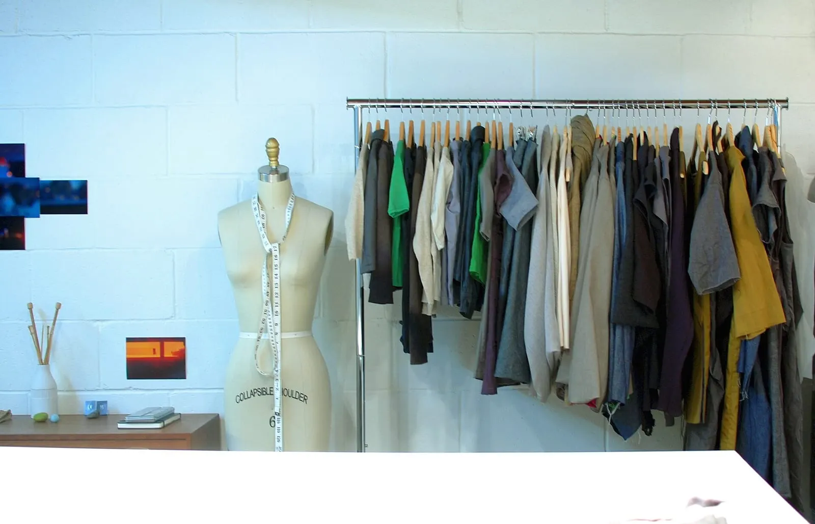 A sewing studio: a dress form with a tape measure around it beside a rail of finished garments